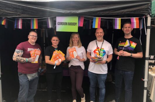 An image of Gordon Moody employees, alumni, and stakeholders in front of the Gordon Moody stand at Manchester Pride in August 2023.